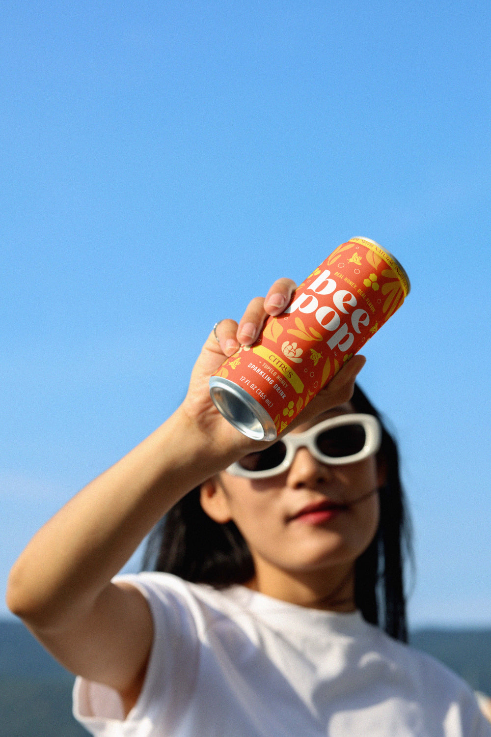 Person holding a red can against a clear blue sky