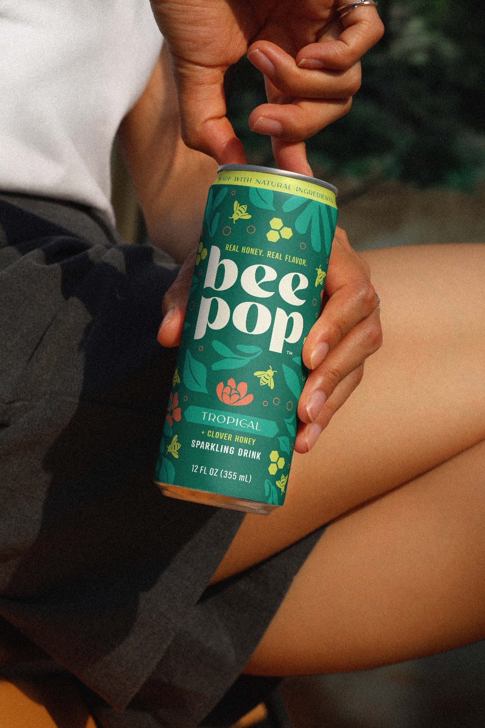 Person holding a can of 'bee pop' drink with a green label.